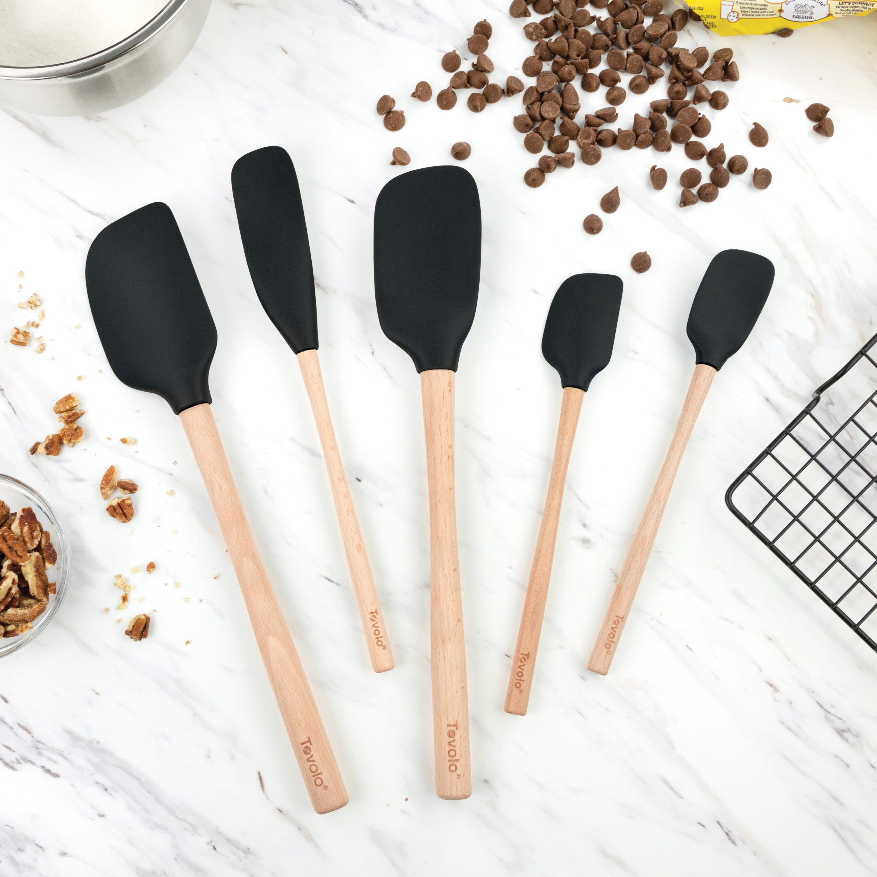 Five Flex-Core Wood-Handle Spatula Set pieces are arranged on a marble countertop, surrounded by chocolate chips, pecans, and a cooling rack for a classic baking scene.