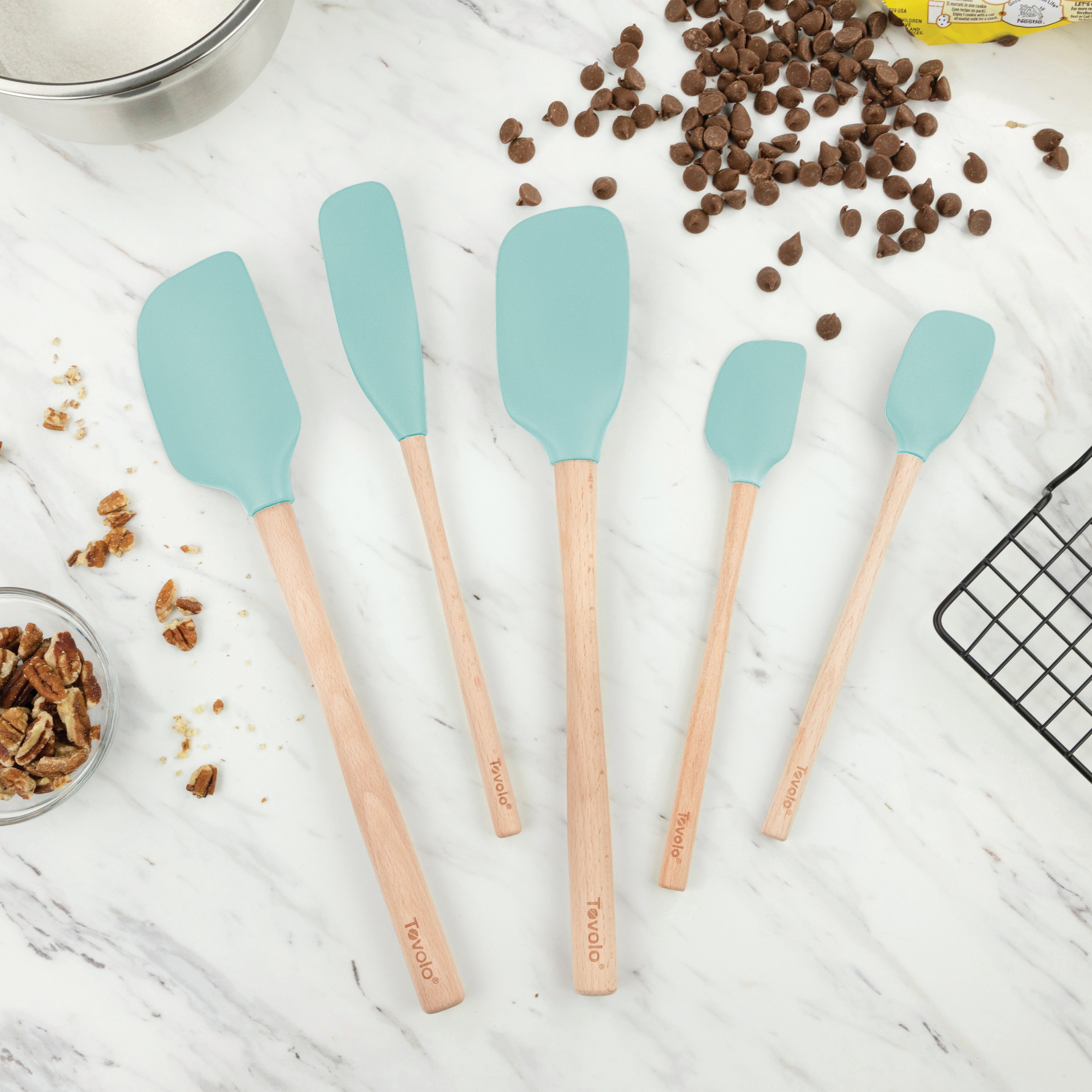 Five Flex-Core Wood-Handle Spatulas from the set of 5 are arranged on a marble countertop, surrounded by pecans, chocolate chips, a wire cooling rack, and a mixing bowl.