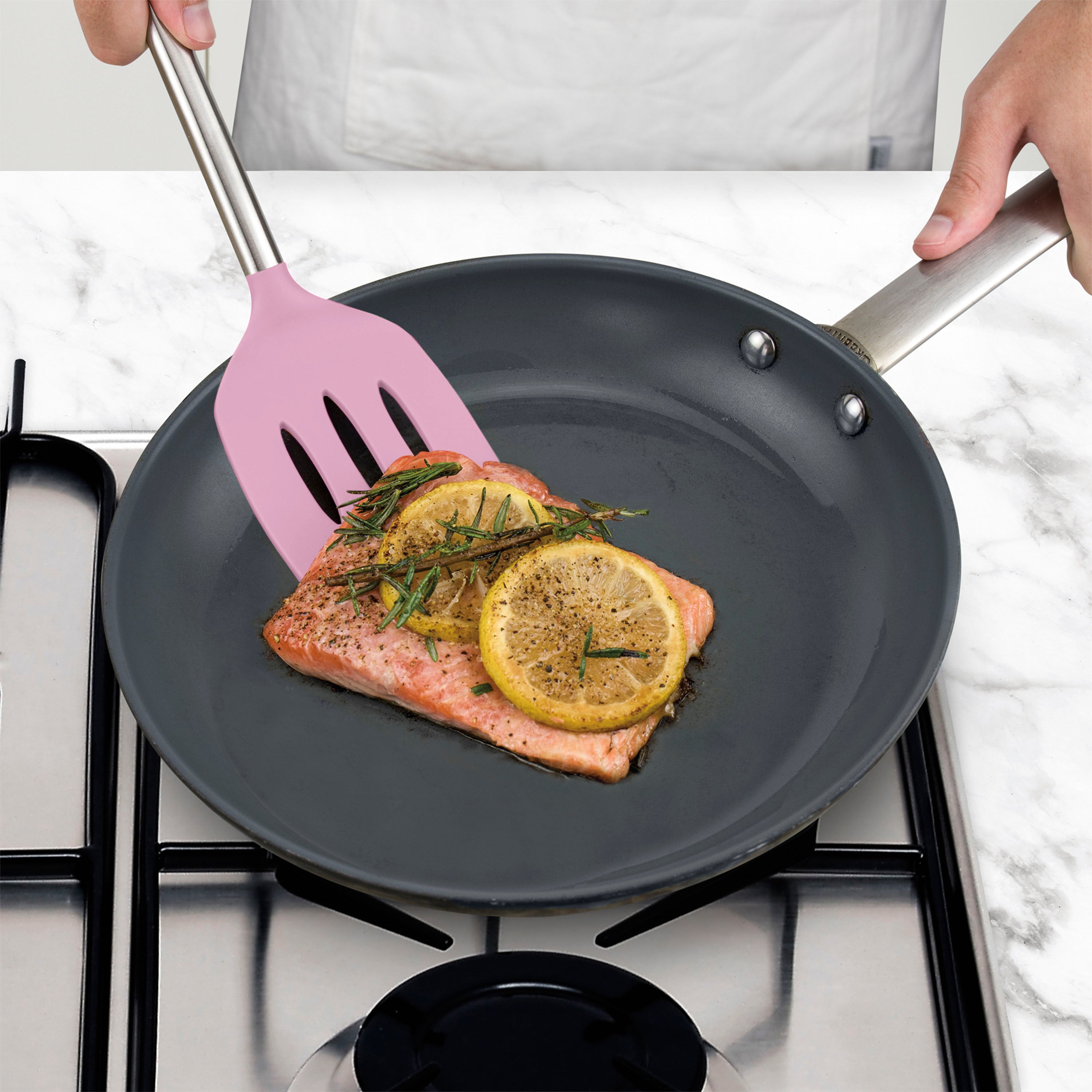 A person cooks a salmon fillet with lemon and herbs in a black nonstick frying pan using a nonstick-safe Silicone Slotted Turner.