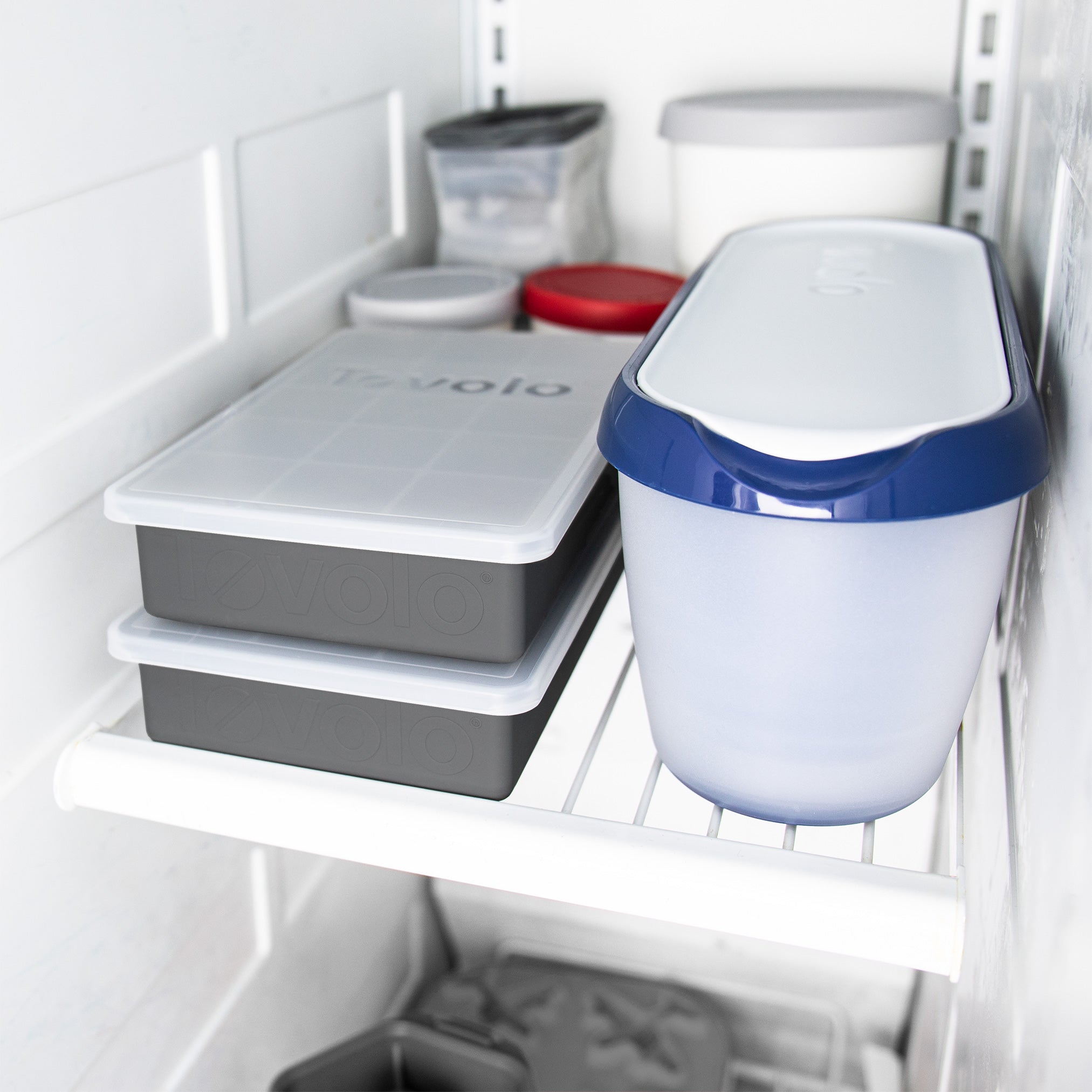 Perfect Cube Ice Mold and assorted plastic food storage containers with lids, in rectangular and round shapes, are neatly organized on a white wire refrigerator shelf.
