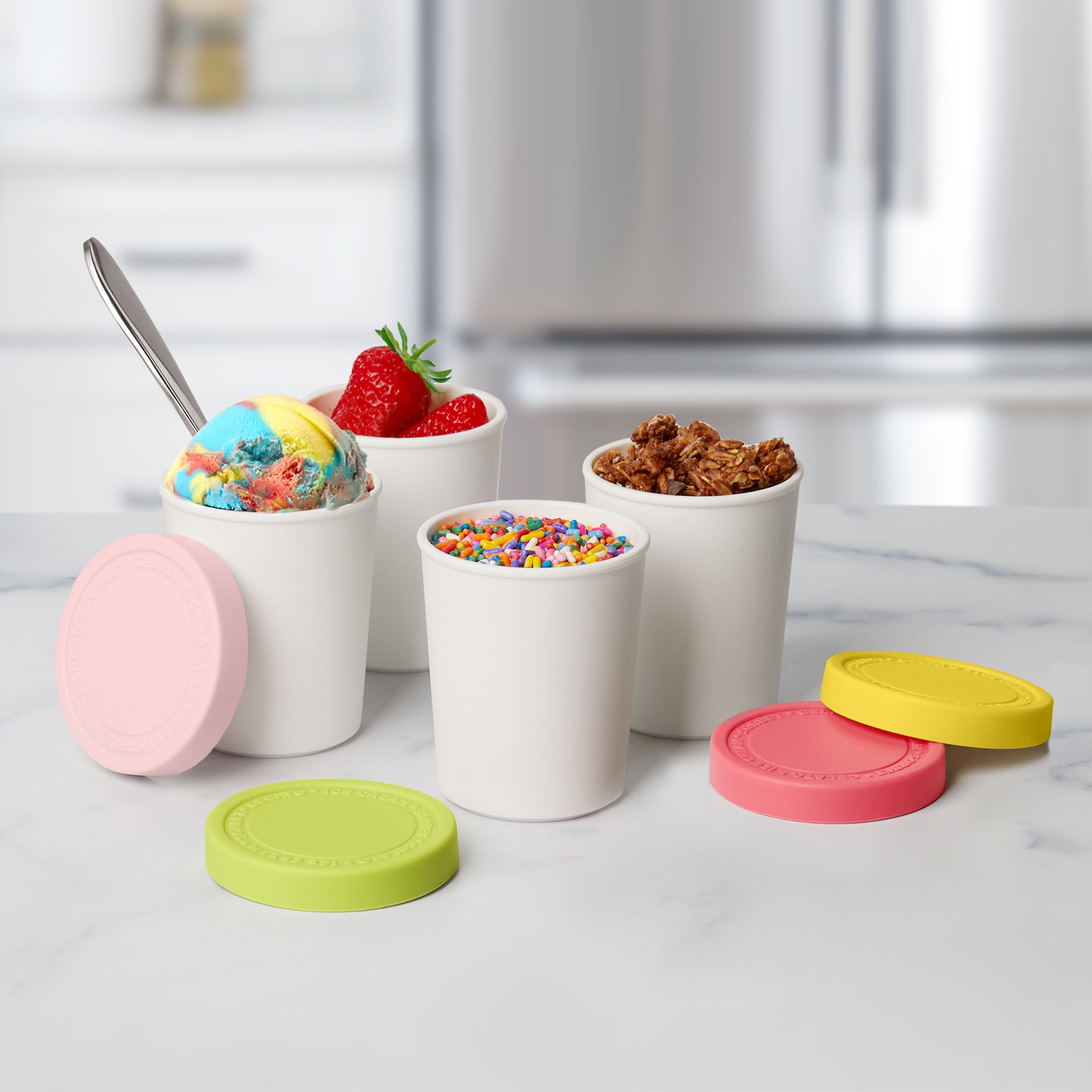 Three white Mini Sweet Treats Tubs on a marble counter hold rainbow ice cream, yogurt with sprinkles, and granola. Pink, green, and red silicone lids beside them help prevent freezer burn on your ice cream favorites.