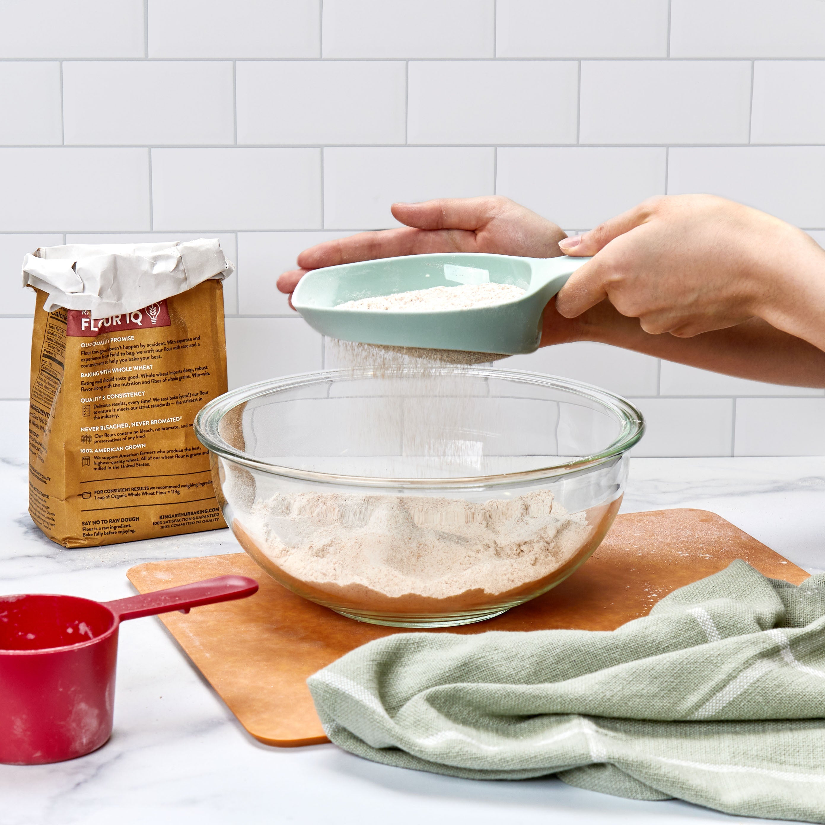 A smiling woman watches as a young girl mixes eggs in a glass bowl with a whisk. Eggs and a bowl of colorful candy are on the kitchen counter in front of them.