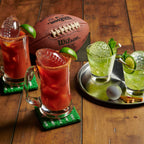 Two Bloody Marys and two mojitos with tovolo Golf and Football Sports Ice Molds (Set of 4) chill on a wooden table, with matching sports-themed coasters, tray, and football and golf ball decor.