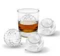 A glass of whisky with a large sports-shaped ice sphere sits beside three matching tovolo Golf and Tennis Sports Ice Molds (Set of 4) and water droplets, all arranged on a white background.