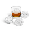 A glass of whiskey with a large, golf ball-shaped ice from the tovolo Golf and Tennis Ice Molds (Set of 4) sits beside three more molds on a white background.