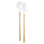 Two white Flex-Core Mini Spat + Spoonula utensils by Tovolo, made of silicone with light wooden handles and the brand name printed at the bottom, are placed side by side on a white background.