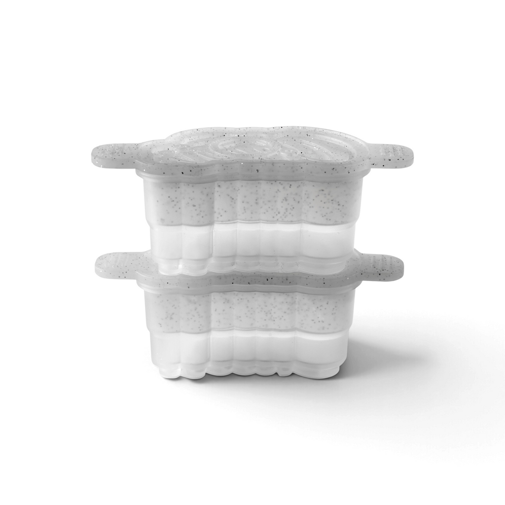 The tovolo Cheers Ice Molds (Set of 2) feature clear containers with speckled, semi-transparent lids, rounded edges, and side grips. Shown stacked, each mold is half-filled with a white substance.