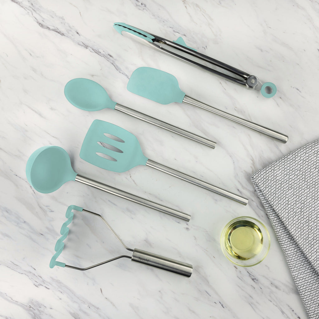 The tovolo Silicone and Stainless Steel Utensil Set of 6 features heat-resistant, non-scratch teal silicone heads and stainless steel handles, displayed on white marble beside a glass bowl of oil and a gray textured cloth.