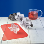 Tovolo Texas Ice Molds (Set of 2) are shown on a white table with a red mat, alongside a glass filled with red liquid. The Texas-shaped molds and blue background create a colorful display.