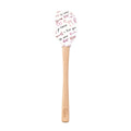 The Spring Spatulart features a wood handle and a white silicone head decorated with red and black handwritten "I love you," "te amo," hearts, and XOXO—perfect for adding a touch of love to your baking.