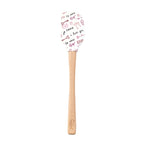The Spring Spatulart features a wood handle and a white silicone head decorated with red and black handwritten "I love you," "te amo," hearts, and XOXO—perfect for adding a touch of love to your baking.