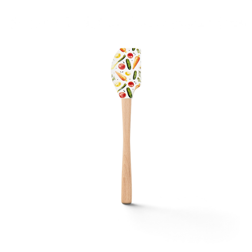 The Spring Spatulart features a wood handle and silicone head decorated with a vibrant carrot patch of tomatoes, carrots, cucumbers, and herbs on a crisp white background.