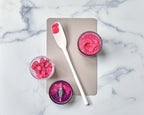 The tovolo Flex-Core Blender Spatula with a long white handle and pink smoothie on it rests on a beige board, surrounded by a jar, blender cup with chopped fruit, and blender blade containing vibrant pink smoothie, atop a marble surface.