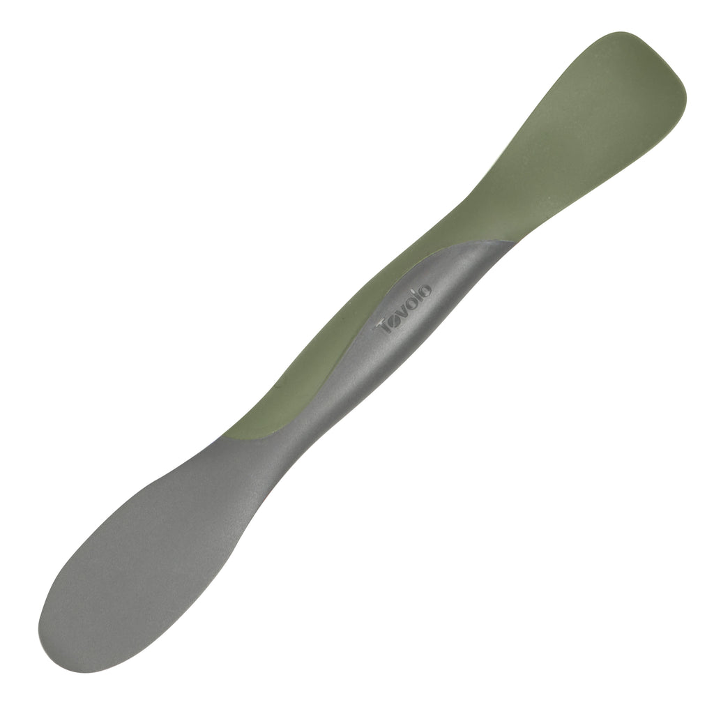 The Scoop and Spread is a double-ended kitchen tool in gray and olive green, shown on a white background. With a broad, flat end for scooping and spreading and a narrower opposite end, it’s the perfect helper for bakers.