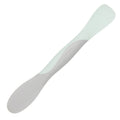The Scoop and Spread is a silicone baby spoon with a grey handle and pale green scoop, designed as a flexible, dual-ended tool for convenient infant feeding.