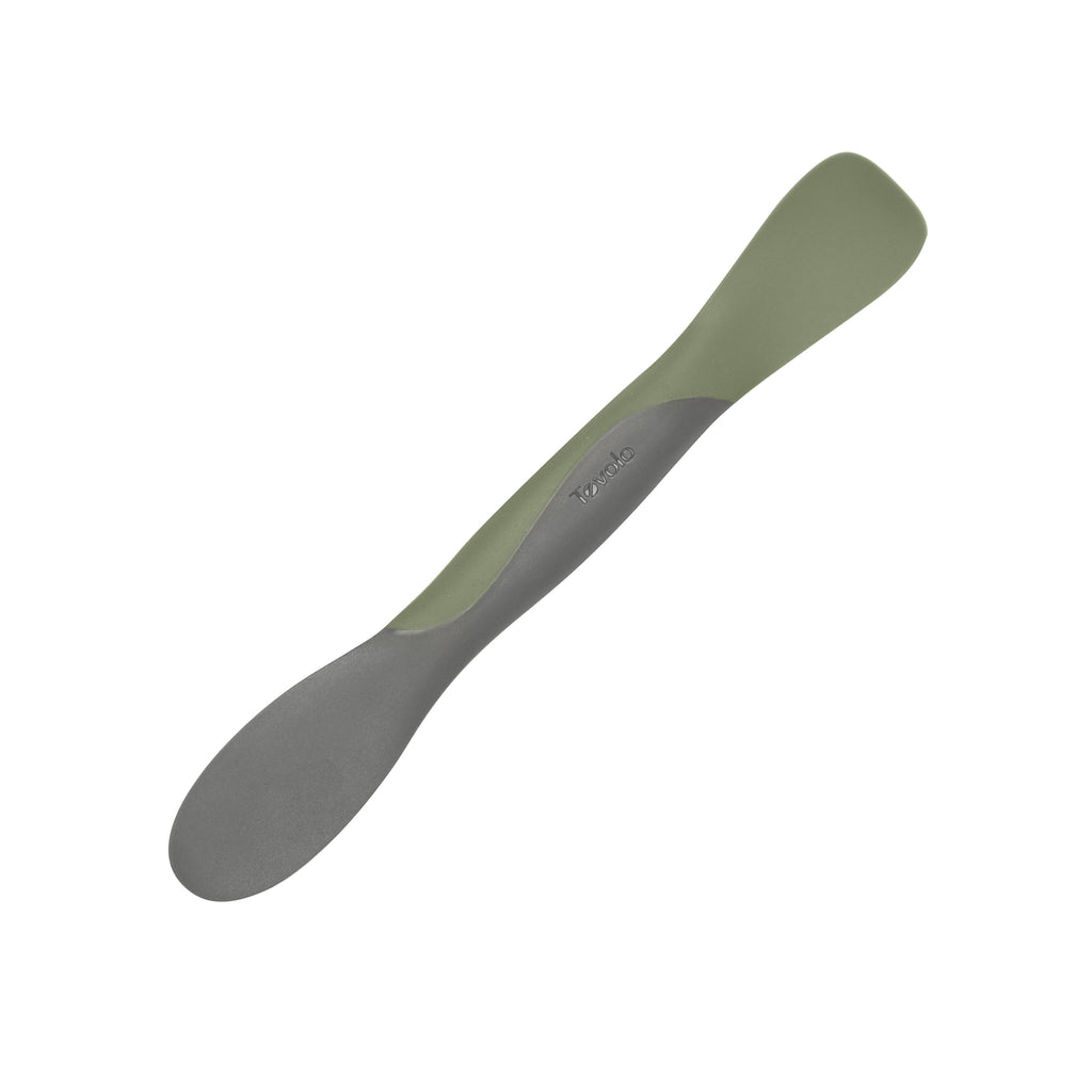 The Scoop and Spread is a dual-ended silicone baby feeding spoon in green and gray on a white background. One end is larger and rounded for scooping, the other is smaller and flatter for spreading, with the Tommee Tippee logo on the handle.