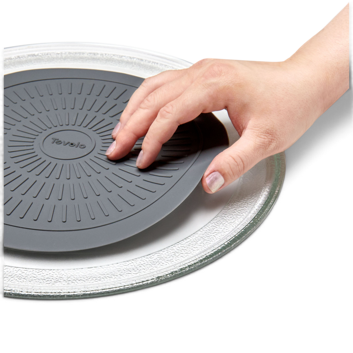 A hand places the round, dark gray Microwave Mat onto a clear glass microwave turntable plate against a white background.
