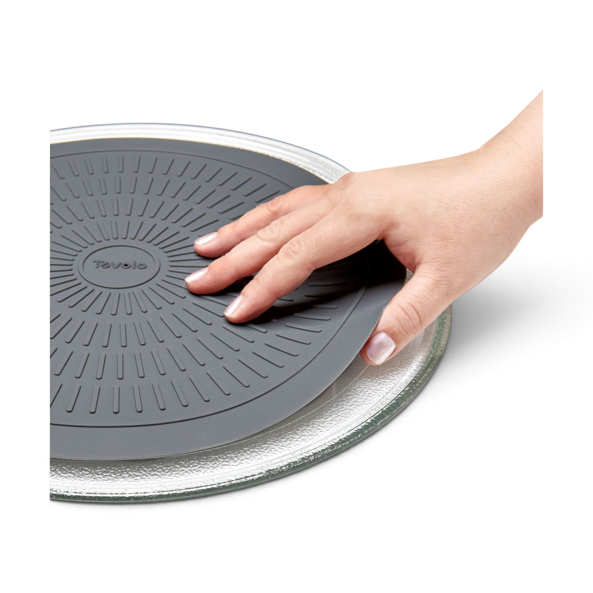A hand places the Microwave Mat, a round gray silicone mat, onto a clear textured glass plate on a white background.
