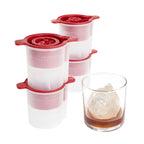 The tovolo Christmas Ornament Ice Molds (Set of 4) with festive red lids are shown beside a glass of whiskey, each making round holiday-themed ice—sleek and perfect as a Christmas gift for cocktail enthusiasts.