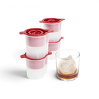 The tovolo Christmas Ornament Ice Molds (Set of 4) with festive red lids are shown beside a glass of whiskey, each making round holiday-themed ice—sleek and perfect as a Christmas gift for cocktail enthusiasts.