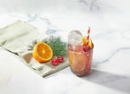 A glass of pink iced drink with orange slices, a cherry, and striped straw sits beside festive tovolo Santa Paws Ice Mold (Set of 2), an orange half, cherries, and a pine branch on a white surface.