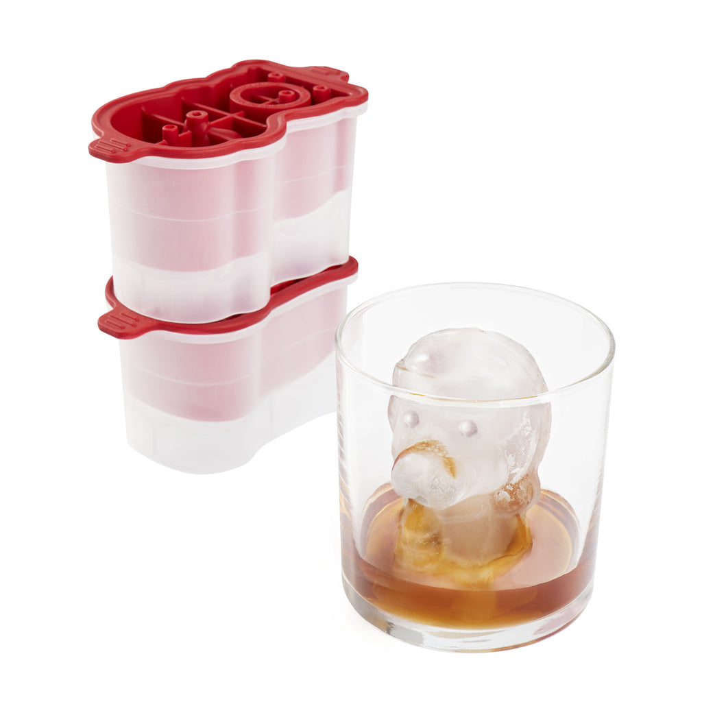 A glass of brown liquor with a large cartoon-shaped ice cube sits beside the tovolo Santa Paws Ice Mold (Set of 2), a festive red and white mold ideal for adding holiday cheer or gifting at Christmas.