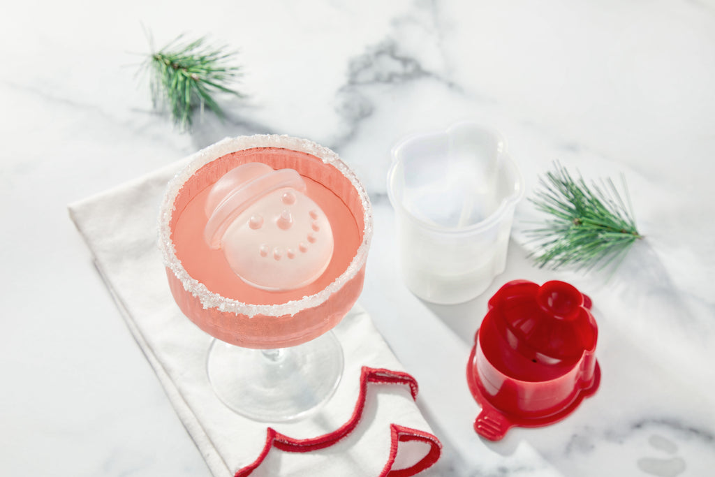 A pink drink in a glass with a sugared rim features a large, smiling snowman ice cube made with tovolo’s Top Hat Snowman Ice Molds (Set of 2)—the perfect festive cocktail accessory for your holiday celebrations.