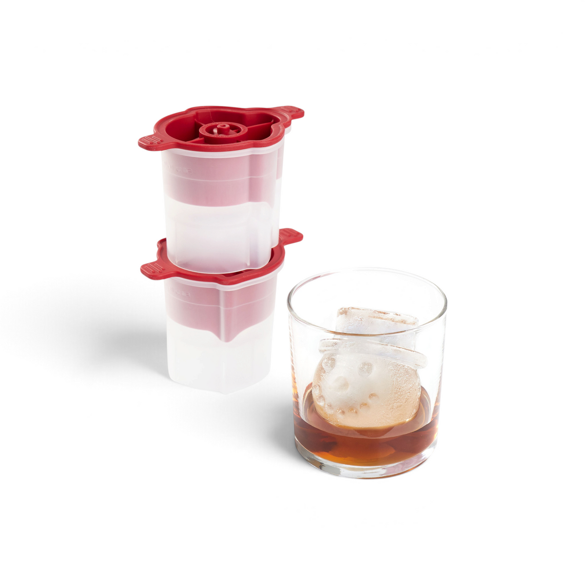 A glass of dark liquid with a slow-melting, snowman-shaped ice cube made using tovolo's Top Hat Snowman Ice Molds (Set of 2) sits in front of two stacked red and white molds.
