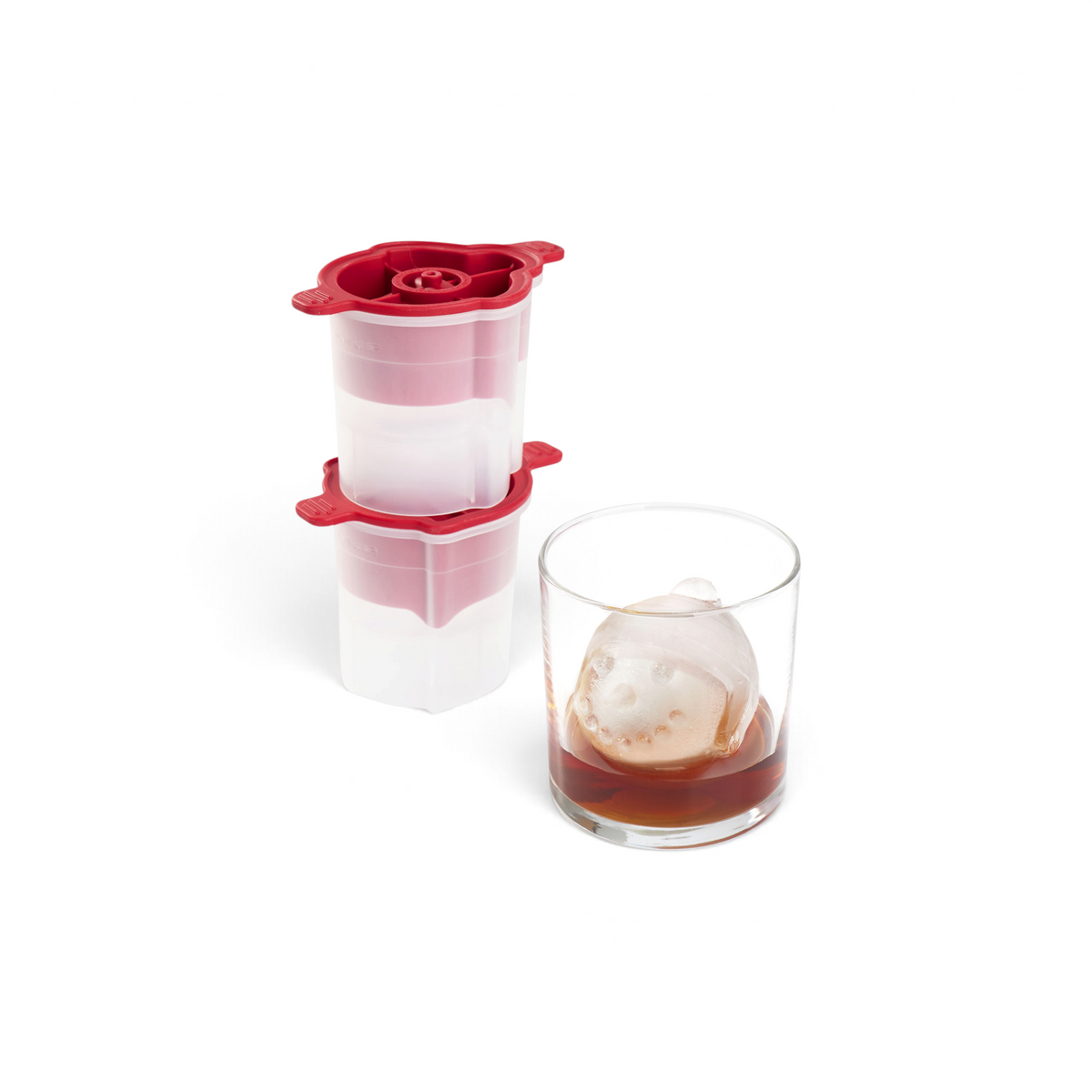 A glass of dark liquor with a clear dog-shaped ice cube and stacked red and white tovolo Holiday Ice Molds—ideal for elevating your holiday cocktails or gifting to any spirits lover this Christmas.