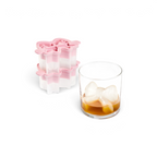A glass with brown liquid and butterfly-shaped ice from the tovolo Fancy Bow Ice Molds (Set of 2) sits beside the pink and white silicone tray.