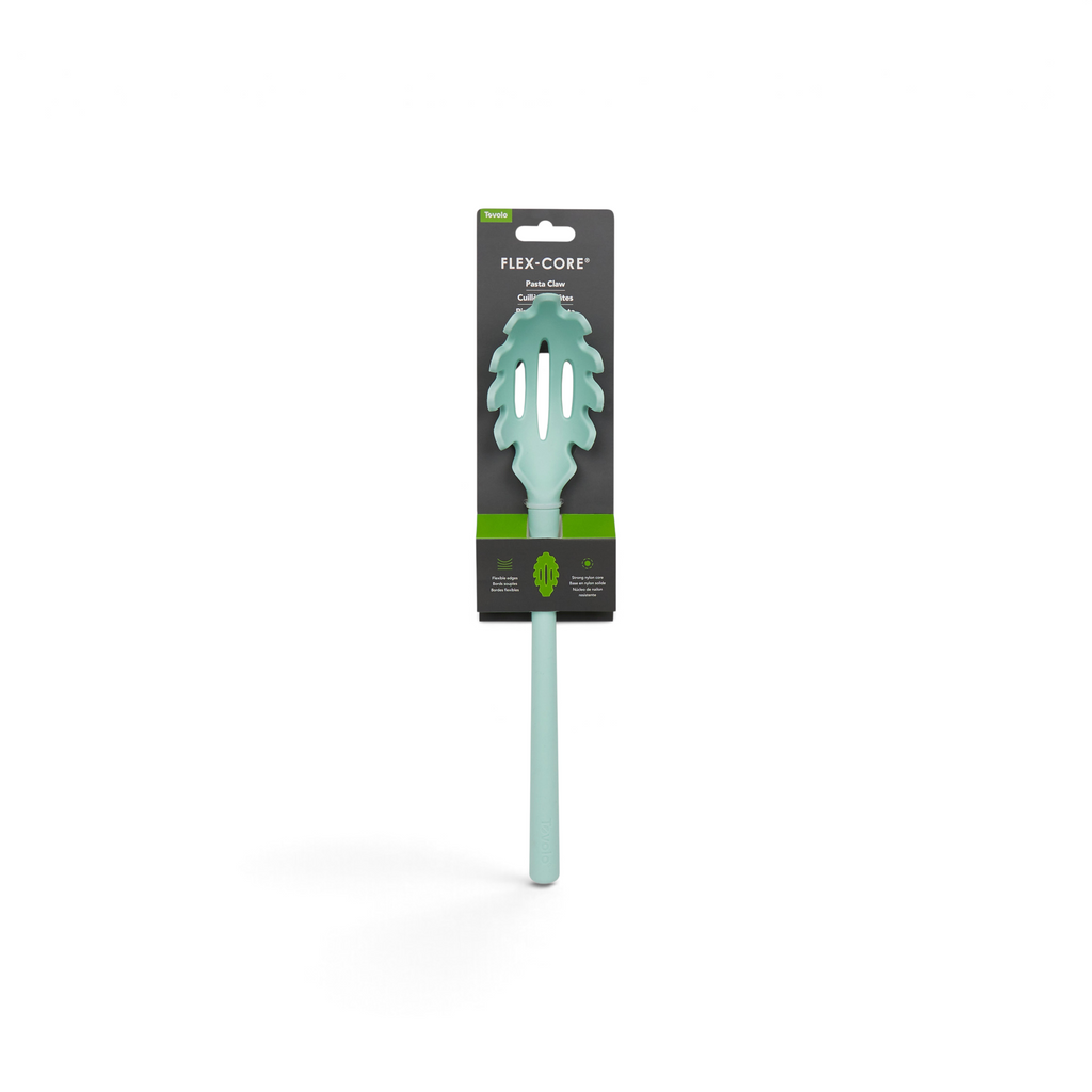 The tovolo Flex-Core Silicone Pasta Claw comes in mint green with a long handle and leaf-shaped cutouts, featuring slotted holes. It is attached to black and green branded packaging labeled “Flex-Core Pasta Claw.”.