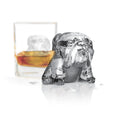 A bulldog-shaped ice cube made with tovolo Dog Ice Molds (Set of 2) rests on a wet surface before a whiskey glass holding another sculpted cube, all set against a crisp, minimal white background.