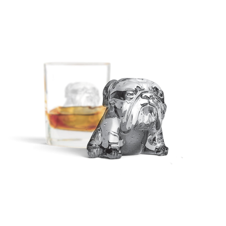 A bulldog-shaped ice cube made with tovolo Dog Ice Molds (Set of 2) rests on a wet surface before a whiskey glass holding another sculpted cube, all set against a crisp, minimal white background.