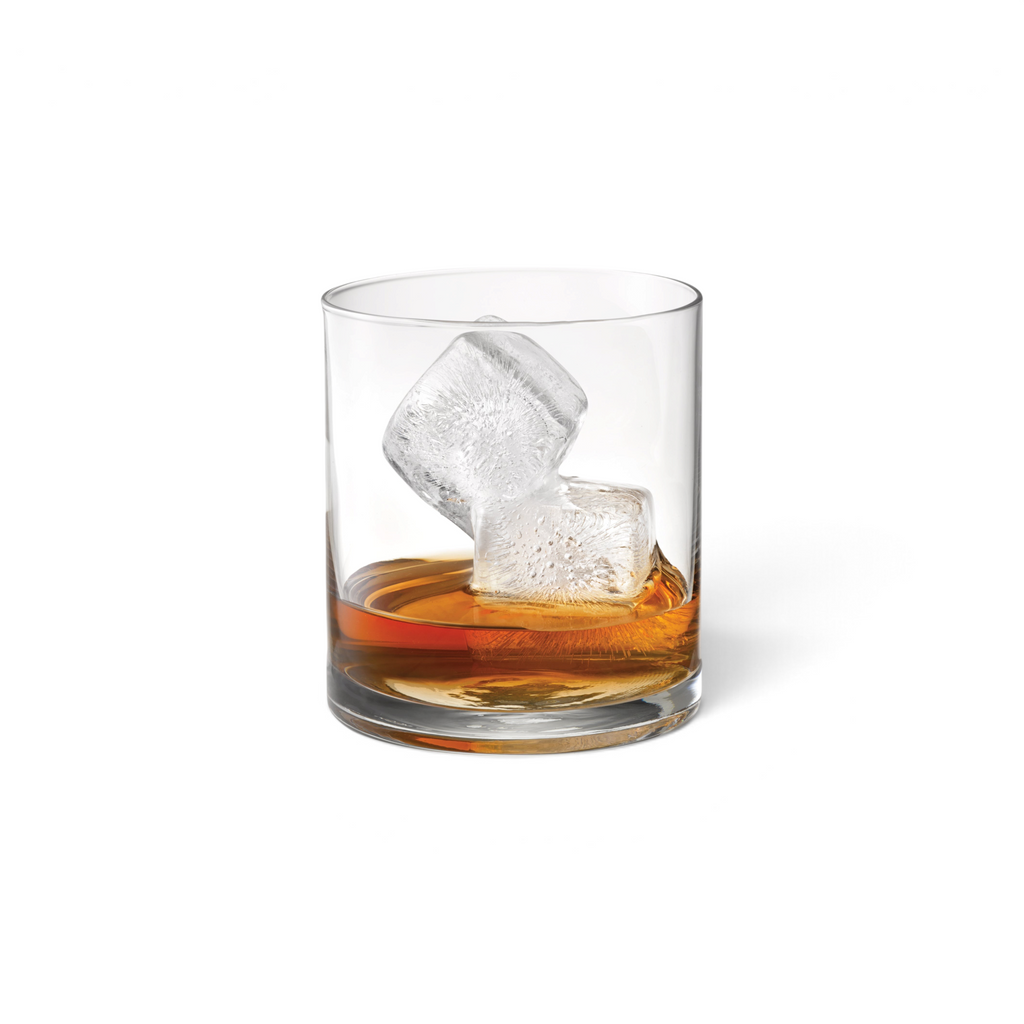 A glass of whiskey with two large, slow-melting cubes made using tovolo Double Rocks Ice Molds (Set of 2) rests on a white background.