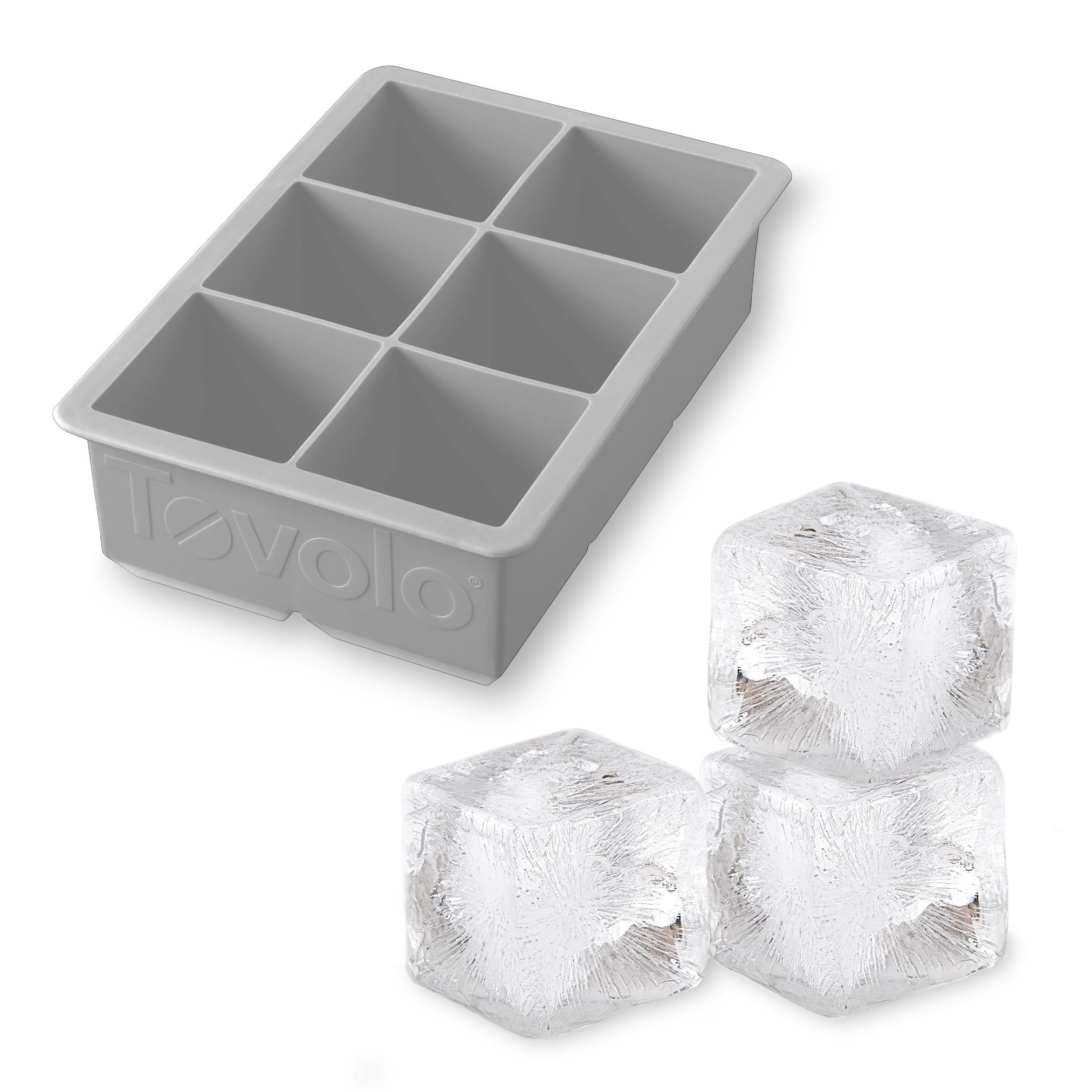 A gray King Cube Silicone Ice Mold by tovolo, featuring six large compartments, is shown beside three clear, square craft ice cubes. The tovolo brand name appears embossed on the side of the tray.