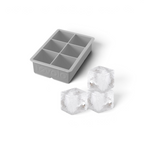 A gray King Cube Silicone Ice Mold by tovolo, featuring six large compartments, is shown beside three clear, square craft ice cubes. The tovolo brand name appears embossed on the side of the tray.