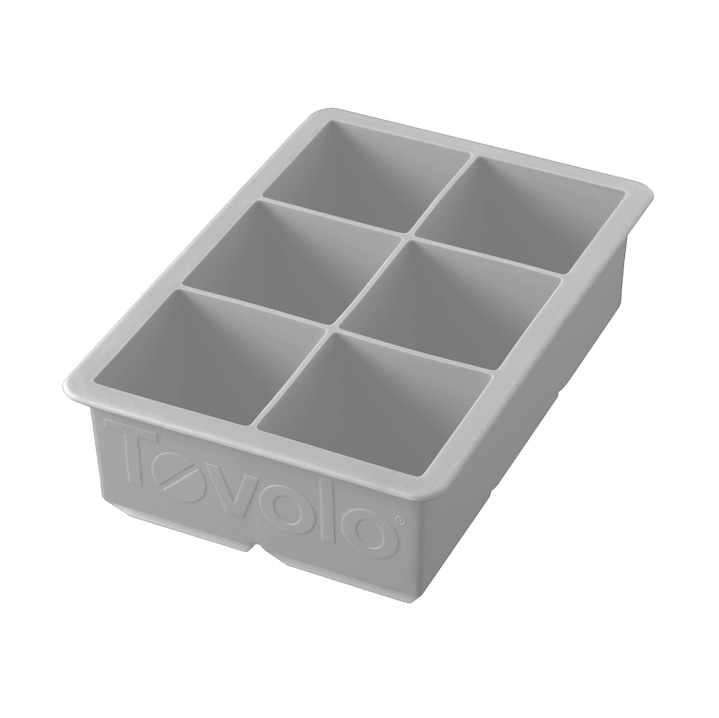 The tovolo King Cube Silicone Ice Mold features six large rectangular compartments, ideal for craft ice. This gray tray is made of silicone and has the tovolo brand embossed on the side.