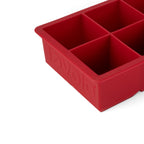 Close-up of a red King Cube Silicone Ice Mold by tovolo with four large square compartments for extra-large ice cubes and the brand name embossed on the side.