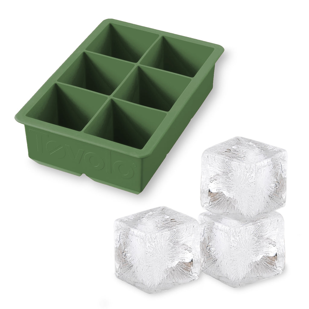 The tovolo King Cube Silicone Ice Mold in green, featuring six compartments, is pictured beside three large, clear ice cubes.