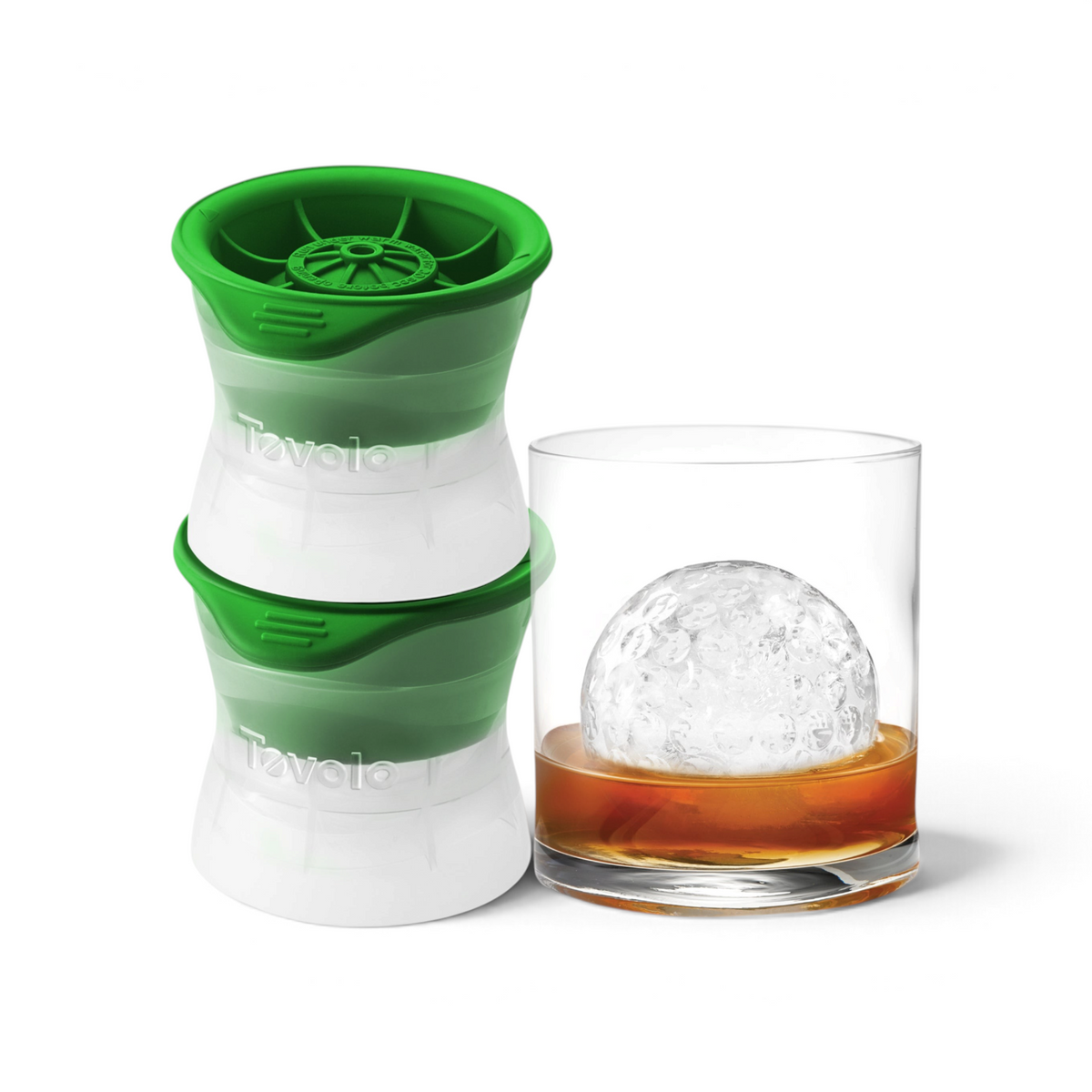 Two green and white Tovolo Baseball Ice Molds (Set of 2) are placed beside a glass of whiskey, displaying a large, clear baseball-shaped ice sphere inside.
