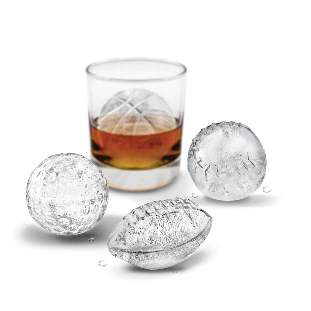 Three sports-shaped ice cubes—a golf ball, baseball, and football—made with Sports Ice Molds are displayed in front of a glass of whiskey with a round ice cube inside, all set against a white background.