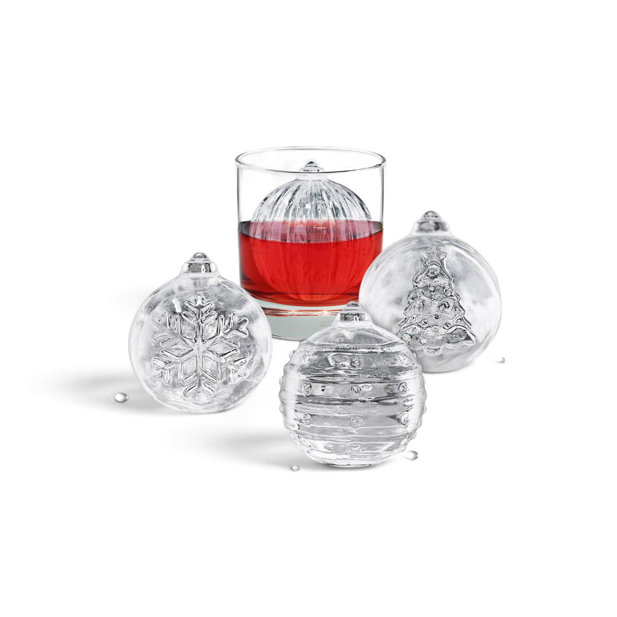 Four round ice cubes made with tovolo Holiday Ice Molds feature festive designs (snowflake, Christmas tree, and stripes). Three sit outside a glass and one is in a red drink—perfect for holiday cocktails or unique Christmas gifts.
