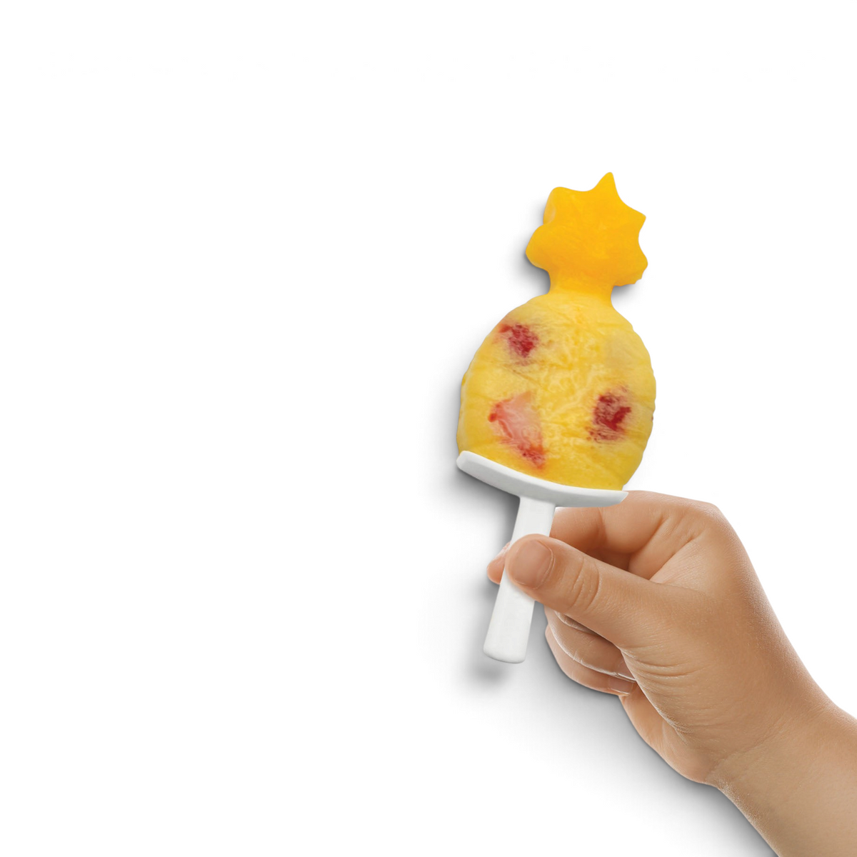 A child holds a pineapple-shaped popsicle with a yellow top and red fruit pieces, made using tovolo Stackable Pop Molds on a white plastic stick, against a white background.