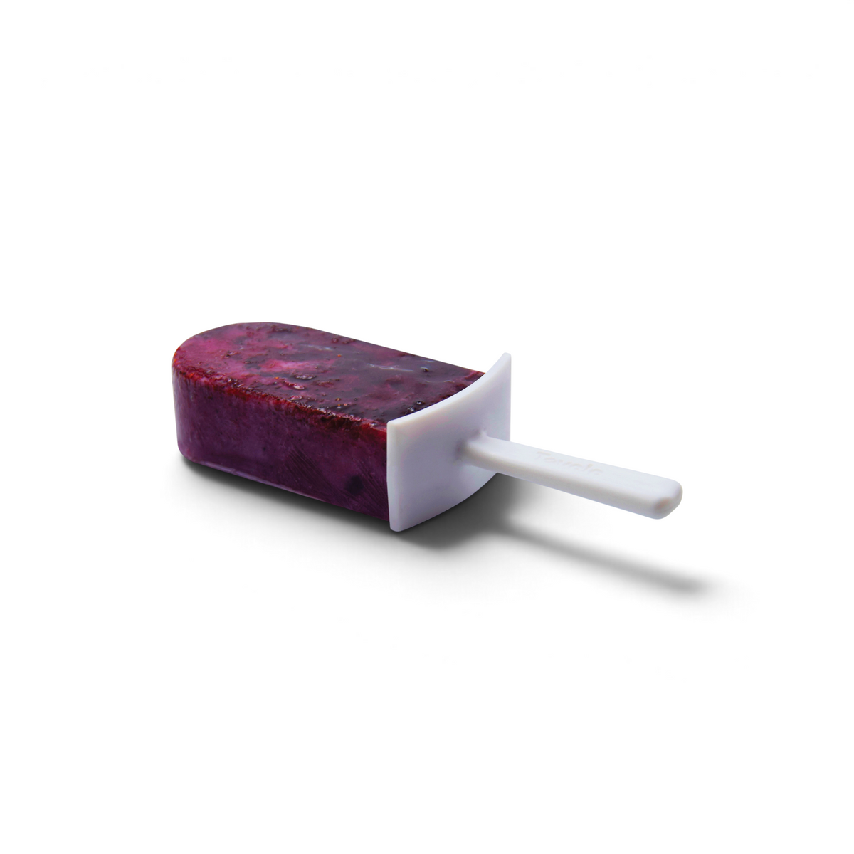 A purple popsicle with visible fruit bits rests on its side in a white holder and stick, made using Stackable Pop Molds, set against a plain white background.