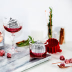 A festive display features cocktails with ornament-shaped spheres made using tovolo's Dots and Stripes Ornament Ice Molds (Set of 2), garnished with herbs and cranberries—perfect for a stylish Christmas gift.