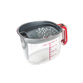 The Gravy Strainer is a clear plastic measuring cup with red markings and a gray silicone lid that features a strainer and pour spout, displayed on a white background.