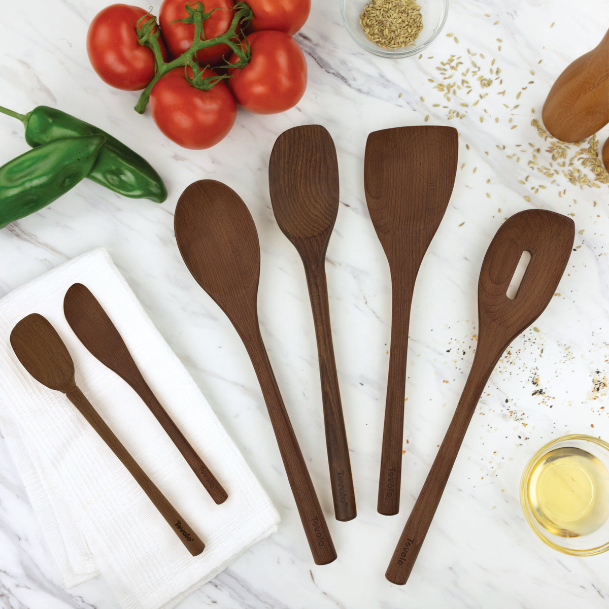 Five Beechwood Utensils, including an angled turner, are arranged on a marble countertop with fresh tomatoes, green peppers, a white towel, a small bowl of oil, and grains—ideal for non-stick cookware.