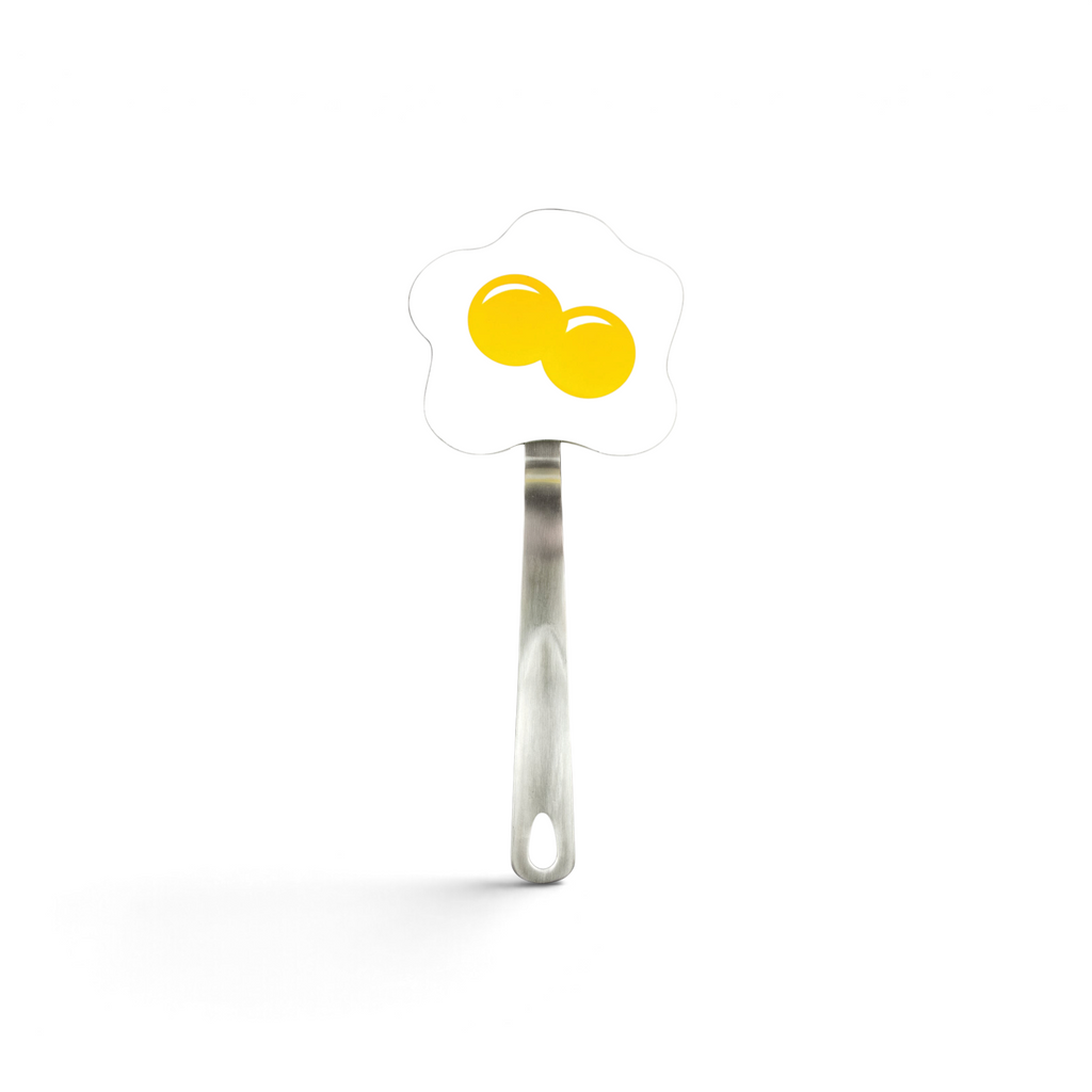 The Spatulart Flex Turner is a nylon spatula with a handle and a flat end shaped like a fried egg, illustrated with two yellow yolks—ideal for use on nonstick skillets.