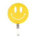 A yellow smiley face sign with a wide, curved smile and oval eyes is mounted on a silver pole, resembling the cheerful design of the Spatulart Flex Turner kitchen tool, which is safe for use with nonstick skillets.