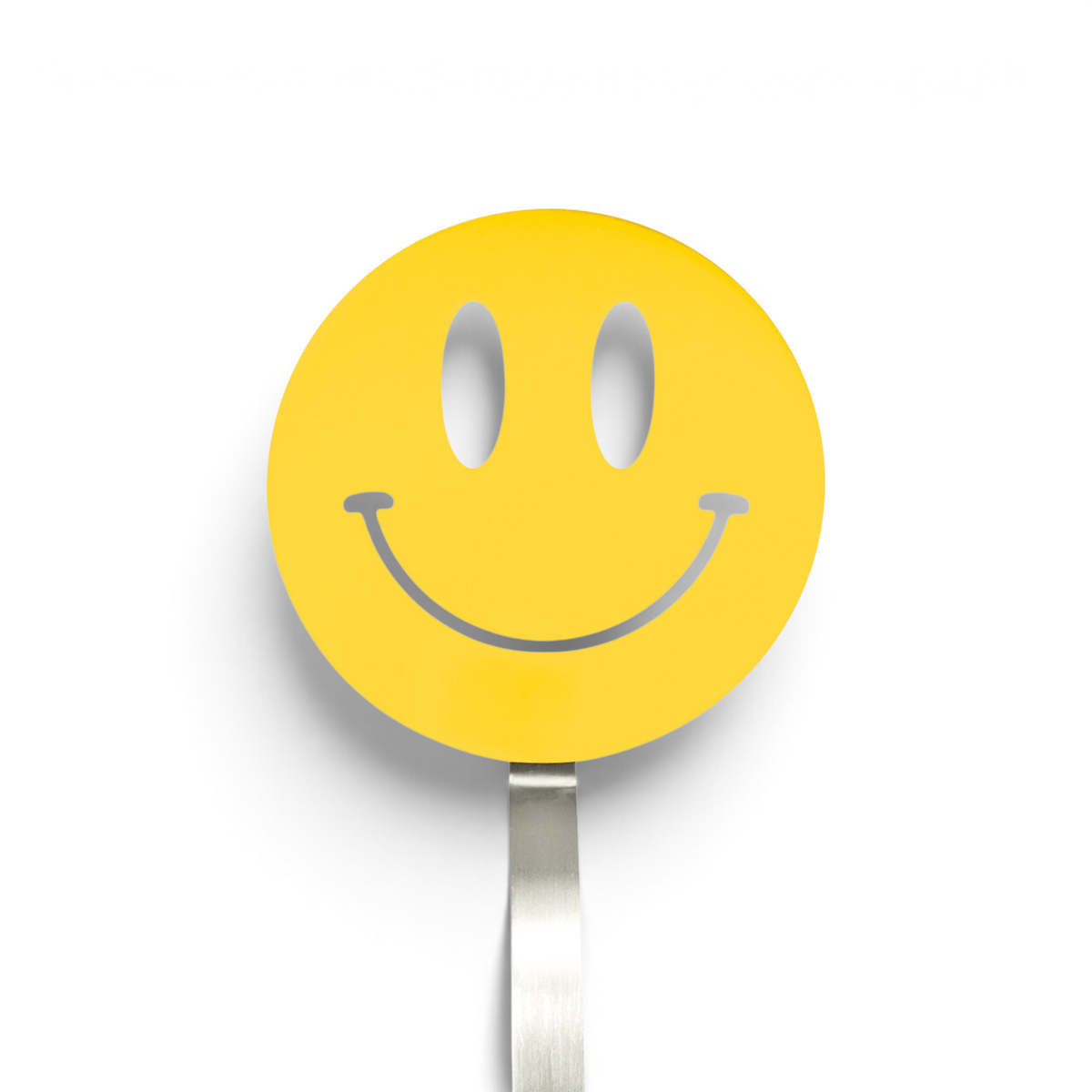 A yellow smiley face sign with a wide, curved smile and oval eyes is mounted on a silver pole, resembling the cheerful design of the Spatulart Flex Turner kitchen tool, which is safe for use with nonstick skillets.